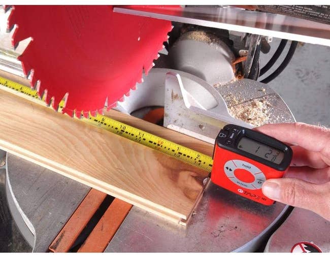 hands using the red digital tape measure to measure a piece of wood