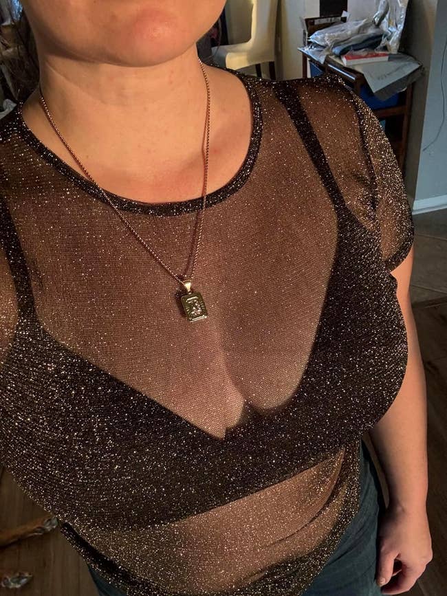 Person wearing a glittery, semi-sheer top with a pendant necklace