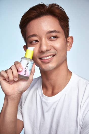 Person smiling, holding a skincare merchandise with a yellowish headdress labeled