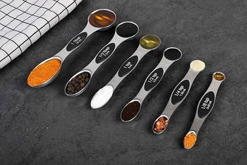 Five measuring spoons with different spices laid out on a textured surface