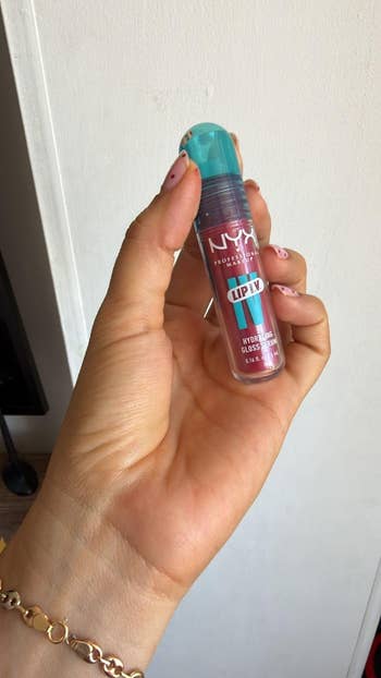 Hand holding NYX Lip Luv Hydrating Gloss, wide   conduit  with a turquoise cap, shown against a plain background