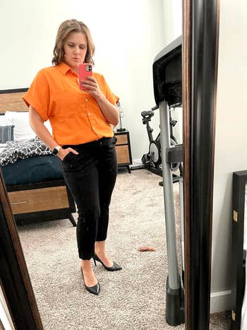 Person in a mirror selfie wearing a bright orange shirt and black pants with pointed black shoes