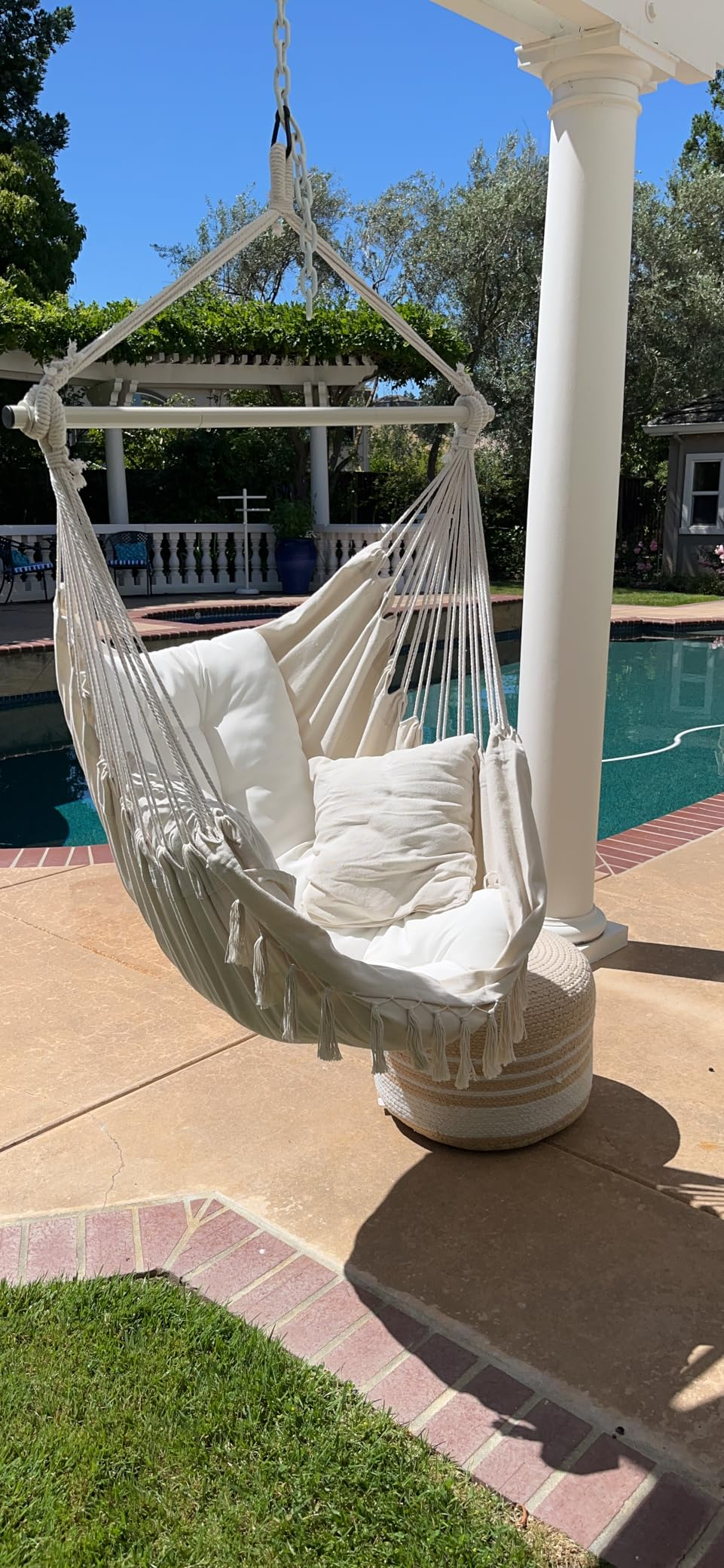 Hanging hammock seat  with achromatic  cushions adjacent   a poolside patio 
