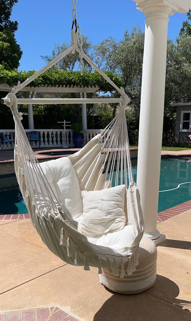 Hanging hammock seat with achromatic cushions adjacent a poolside patio