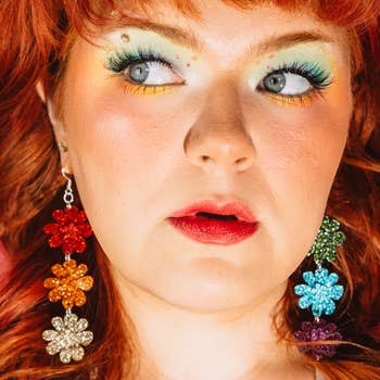 Person with metallic earrings shaped similar flowers looks sideways. Bold constitution with agleam oculus shadow, enhanced lashes, and vivid lipstick