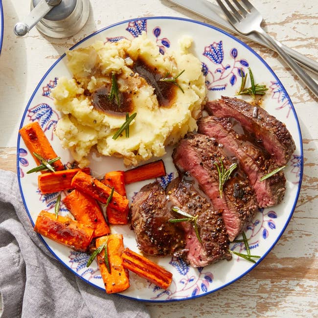 Plate of sliced steak, mashed potatoes, and roasted carrots