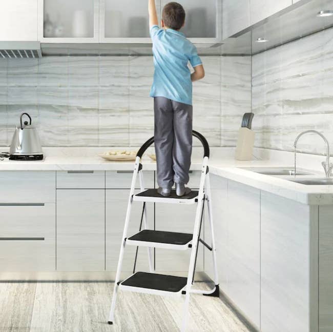 a young person standing on the step ladder in a kitchen