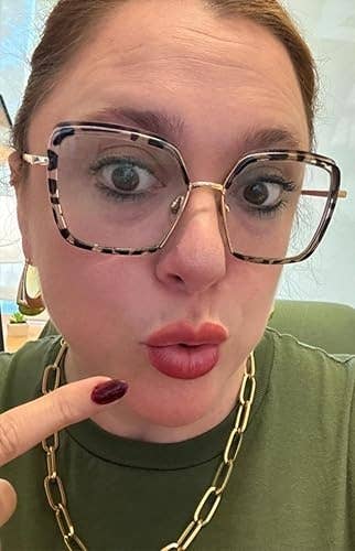 Person with ample  glasses and golden  concatenation  necklace playfully points to lips portion    looking astatine  the camera