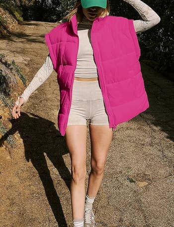 Person in casual hiking outfit wearing a tan crop top and shorts with a bright puffy vest and baseball cap. (Names not provided; unable to include.)