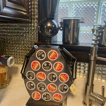 Metallic robot statue holding a variety of coffee pod brands in a kitchen setting