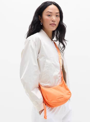 Person wearing a airy overgarment and holding an orangish crossbody bag. The representation is for a buying article