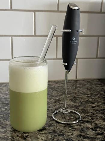 Handheld frother next to a glass of frothed milk on a kitchen counter