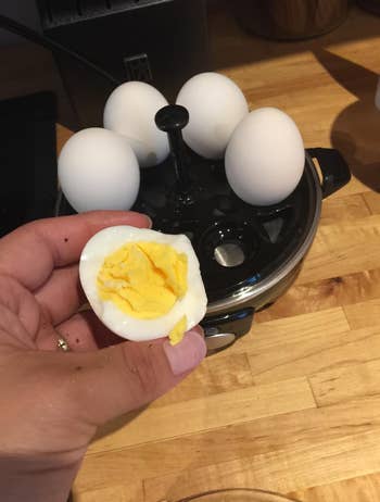 reviewer showing the inside of a perfectly cooked hard boiled egg with the black rapid cooker behind it