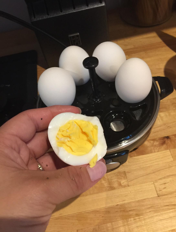 reviewer showing the inside of a perfectly cooked hard boiled egg with the black rapid cooker behind it