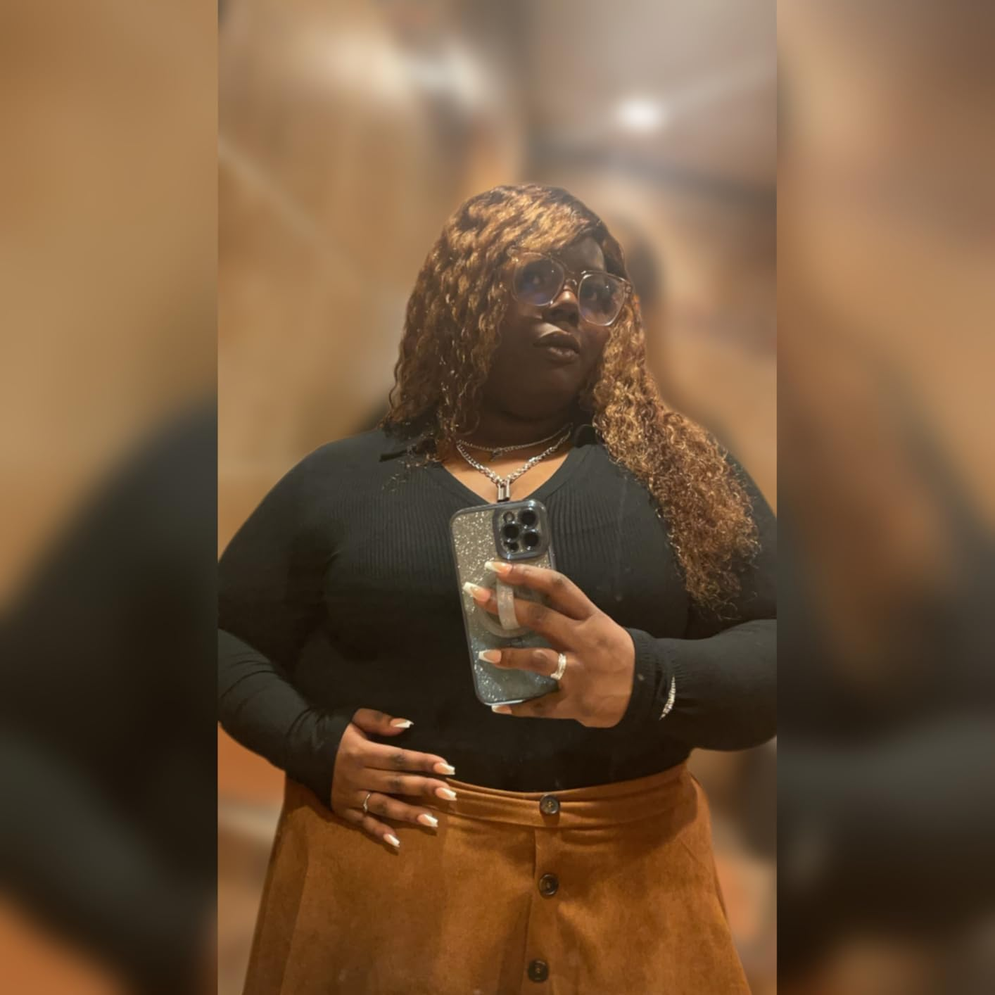 Person taking a mirror selfie wearing a black top and skirt, with sunglasses and curly hair. App is open on smartphone