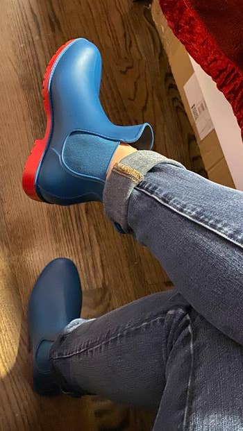 Person sitting with one blue and red shoe on, another shoe off to the side, wearing jeans
