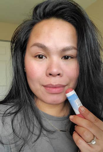 reviewer holding up the pink stick to their face, which has the color applied to their eyelids, cheeks, and lips