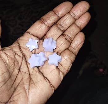 Hand holding small, star-shaped, light-colored wax melts