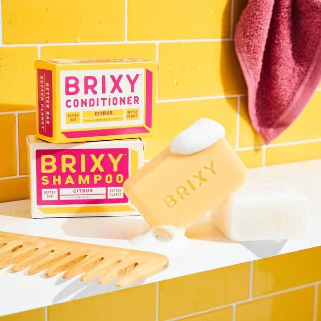 Eco-friendly BRIXY shampoo and conditioner bars on bathroom shelf with towel