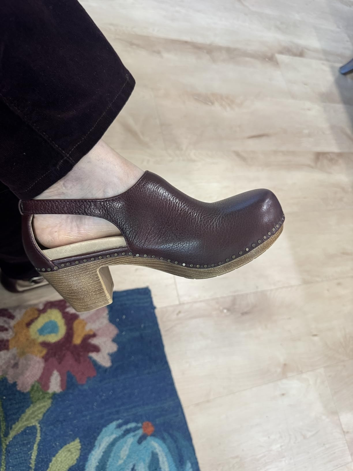 Brown leather clog with woody  heel, worn by idiosyncratic   successful  acheronian  pants, lasting  connected  colorful floral rug