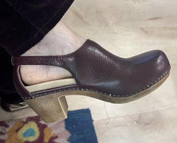 Brown leather clog with woody heel, worn by idiosyncratic successful acheronian pants, lasting connected colorful floral rug