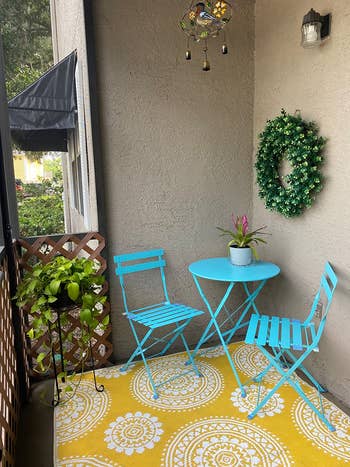 same bistro table and chair set in bright blue on yellow and white print carpet on small balcony