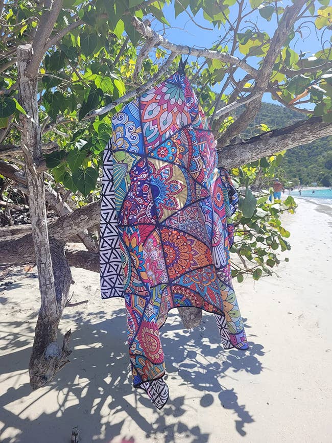 reviewer's patterned fabric beach towel on a tree branch at a beach