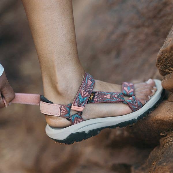 Person wearing geometric-patterned sandals with adjustable straps, stepping connected  a rocky surface, highlighting outdoor footwear for shopping