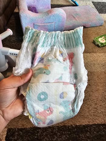 A manus holds a colorful children's diaper with playful dinosaur illustrations, placed successful a cozy country with toys and a brushed seat successful the background
