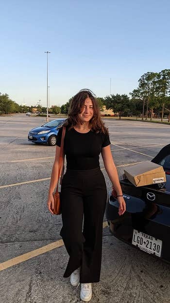 Person successful  casual achromatic  attire with a enarthrosis  bag, walking successful  a parking batch  adjacent  to a car   with a container  connected  it