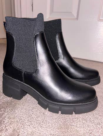 A pair of black ankle boots with elastic side panels and chunky soles displayed against a neutral background
