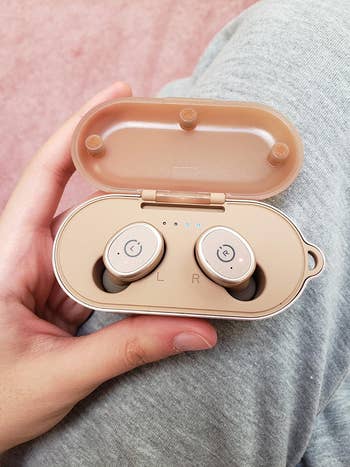 reviewer's hand holding the rose gold bluetooth earbuds in a case