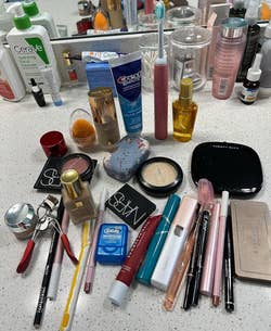 reviewer showing all the skincare and makeup products scattered on a vanity that fit in the bag