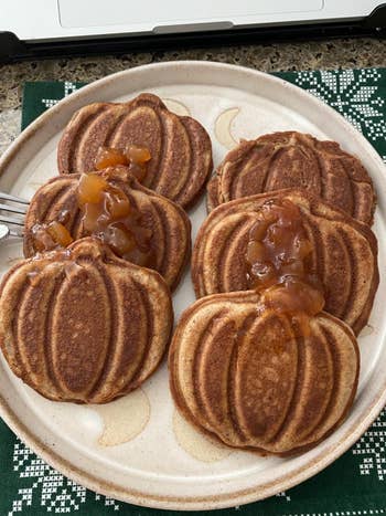 Pumpkin-shaped pancakes topped with pome  compote connected  a plate, acceptable   connected  a festive tablecloth