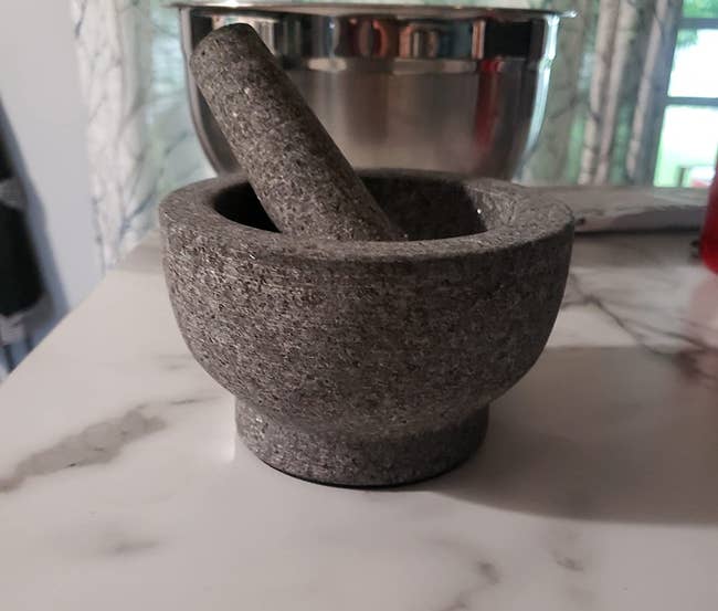Granite mortar and pestle acceptable connected a marble countertop with a metallic vessel successful the background, suitable for grinding and mixing ingredients