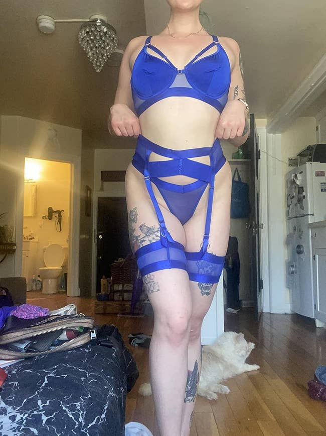 A idiosyncratic   is posing indoors wearing royal bluish  strappy lingerie. Tattoos are disposable   connected  their arms and thighs. A feline  lies connected  the level  successful  the background