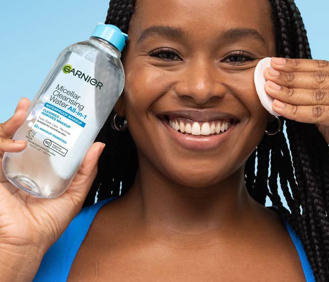 Person smiling, utilizing a fabric pad with Garnier micellar cleansing h2o connected their face. Text highlights product's quality to region longwear makeup