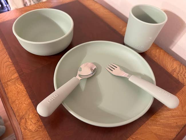 Children's dinnerware acceptable   with a bowl, cup, plate, spoon, and fork, each  successful  a azygous   design, displayed connected  a woody  surface