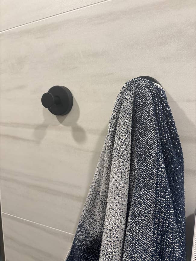 A textured towel hangs on a round black bathroom hook mounted on a tiled wall