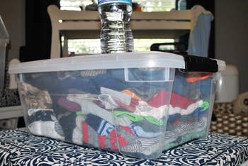 Clear integrative bin filled with folded apparel and topped with a h2o bottle, placed connected a patterned surface