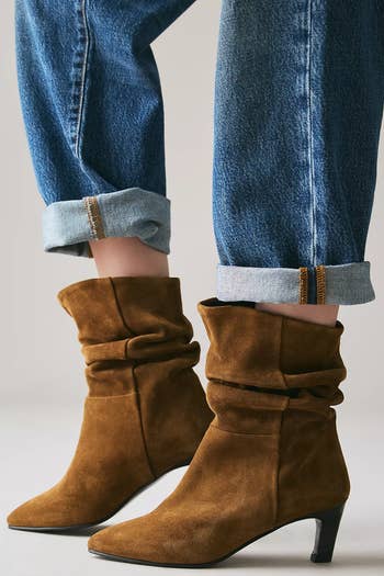 Person wearing rolled-up jeans with brownish  slouchy suede ankle boots, featuring debased  heels