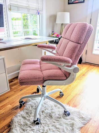 Plush office chair with cushioned armrests on a hardwood floor, next to a desk and window with a view outside. Ideal for comfortable home office setups