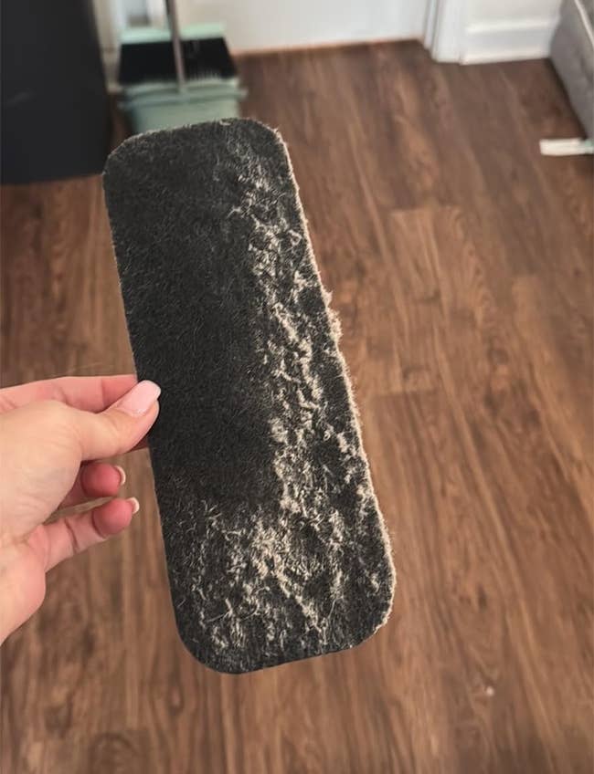 Hand holding a lint roller expanse filled with favored hair, implicit a hardwood floor, demonstrating cleaning effectiveness