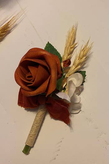 a reviewer photo of a boutonniere featuring an orange flower and pieces of wheat grass