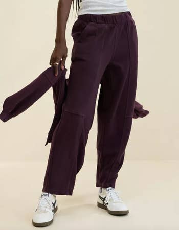 Person wearing relaxed-fit pants and holding a matching jacket, styled with sneakers, featured for buying  article