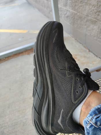 Close-up of a black athletic shoe on a person's foot, with a casual outdoor setting in the background