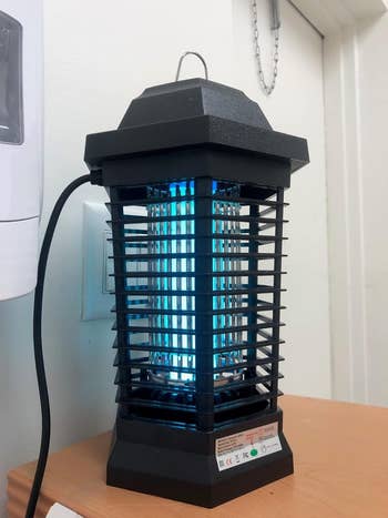 Electric bug zapper with a rectangular design, featuring horizontal and vertical bars; plugged successful  and placed connected  a array  indoors