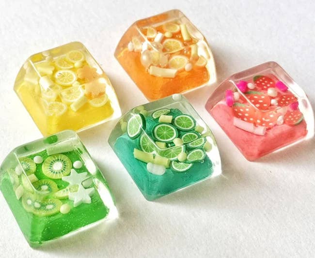 five acrylic keycaps with tiny fruits inside each one