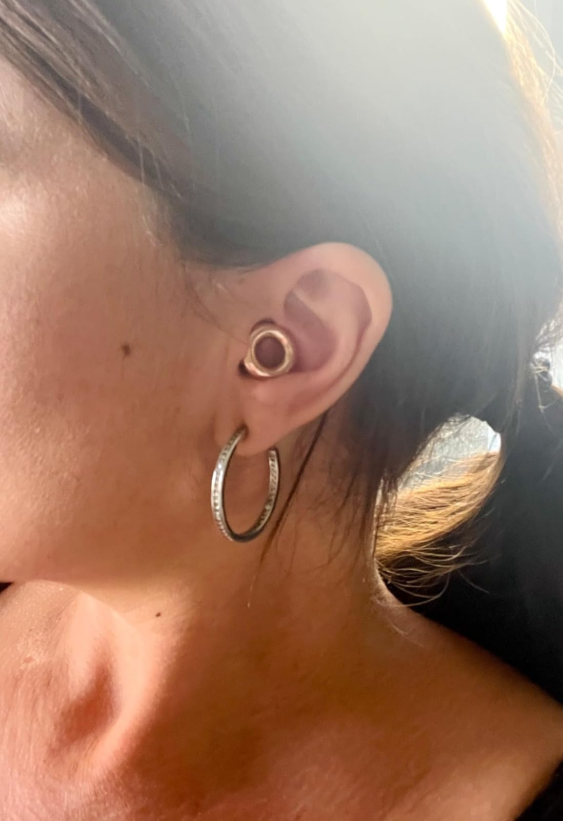 Close-up of a person's receptor  wearing a tiny  circular  receptor  plug and ample  hoop earring
