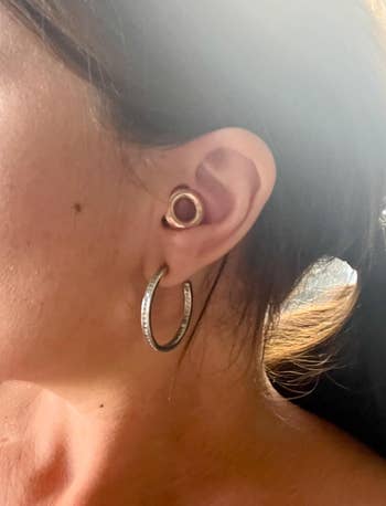Close-up of a person's receptor wearing a tiny circular receptor plug and ample hoop earring